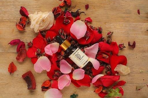 This is an image of a bottle of natural plant oil surrounded by pink, red, and white rose petals.