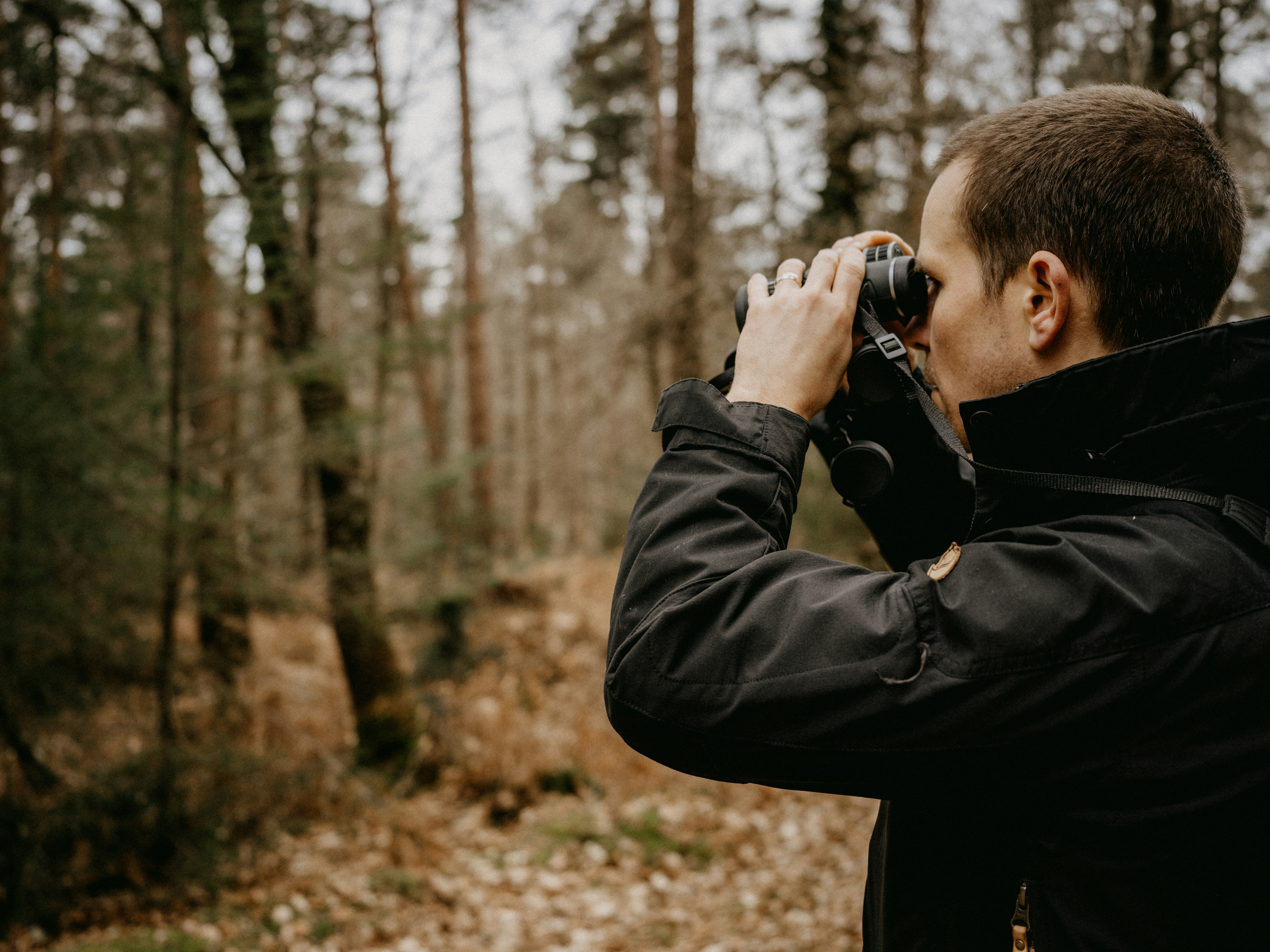 man looking through binoculars into a forest