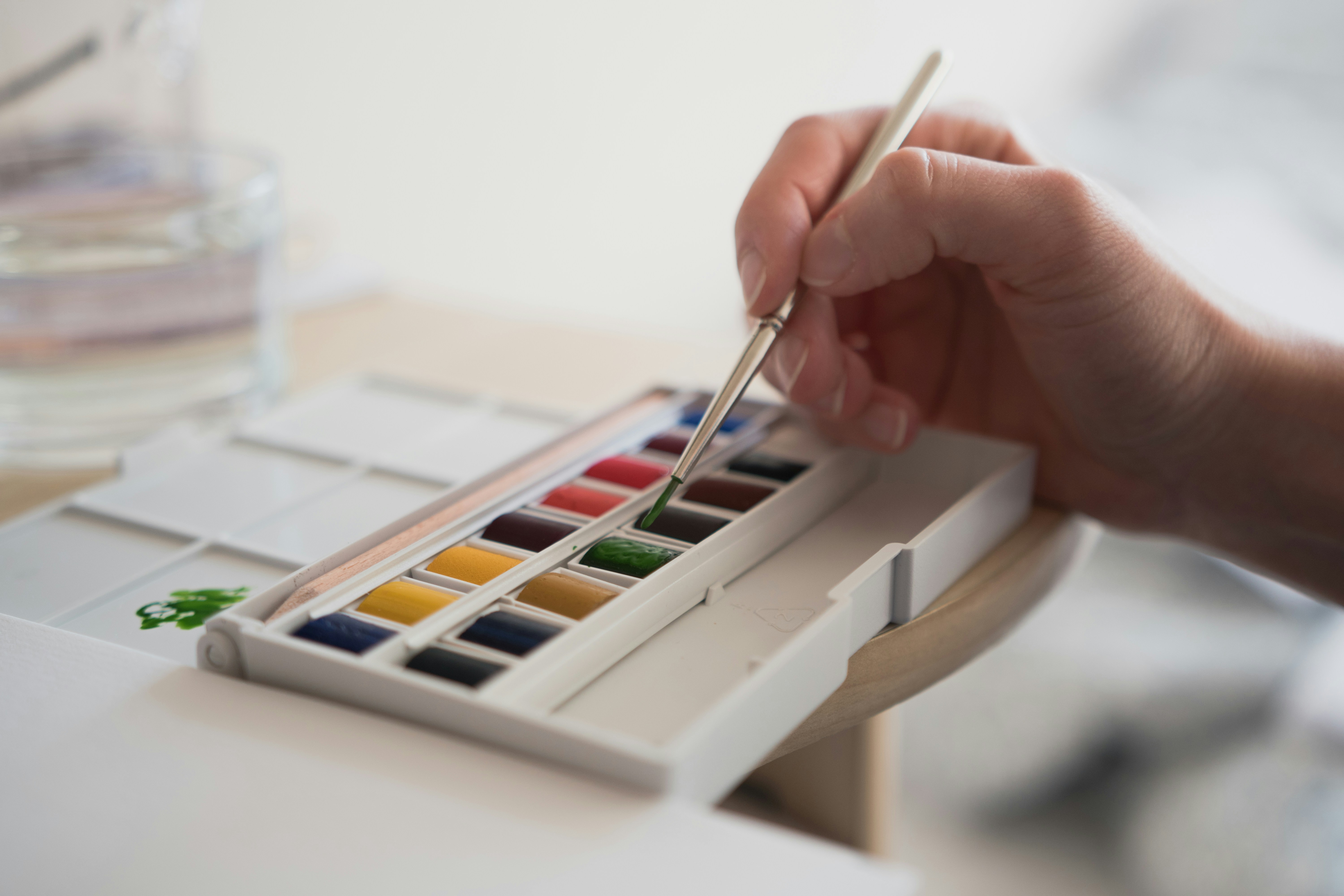 pallet of watercolors with person holding brush dipping into colors