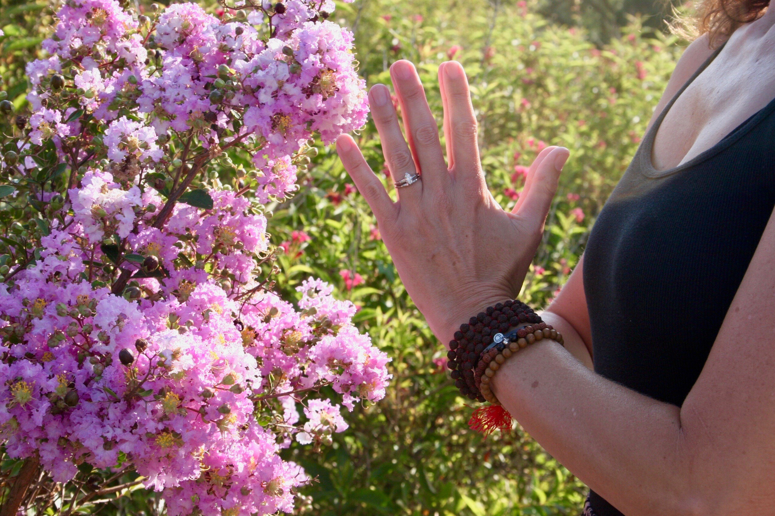 woman posed in yoga stance with hands together in front of pink flowers